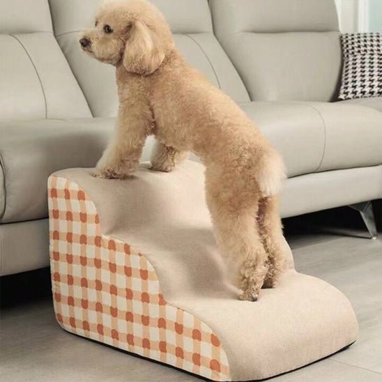 Escalier-mousse-pour_chien-chiot-antidérapant, déhoussable lavable en machine avec mousse haute résilience à mémoire de forme pour protÚger les articulations sensibles, sécurisé , confortable, résistant aux griffes pour petit et chien de moyenne taille-design velours sur le dessus ultra-doux et tissu en coton solide avec motif orange à carreaux style vichy-un petit chien qui monte confortablement sur l'escalier de 3 marches en mousse pour monter sur le canapé du salon en toute sécurité