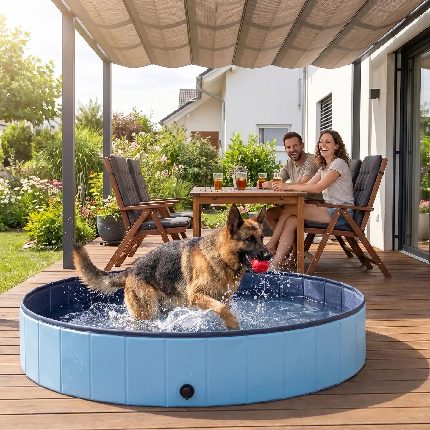 Piscine-pour-gros-chien-rigide-xxl, panneaux MDF robuste anti-affaissement, pliable et lavable de diamètre 160 cm et de 30 cm de hauteur étudié pour une entrée et sortie facile et sécurisé pour le chien avec bouchon de vidange pratique et rapide, polyvalente piscine à balle, bassin, baignoire pour toilettage-unBerger allemand qui court heureux avec sa balle rouge dans la machoire dans la grande piscine robuste pour chien sous le regard des ses maitres souriants qui boivent leur thé glacé sur la terrasse