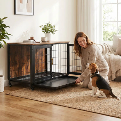 Cage-chien-interieur-avec-4-roues-mobiles rotative à 360° avec freins de sécurité, en bois et acier de couleur noir mat, meuble rectangulaire design moderne et épuré, double porte avant avec serrures robustes à point pour chien et chiot de petite à moyenne taille, de 0 à 30 kg maximum-une propriétaire de chien qui installe en souriant à son chien le fond en forme de plateau amovible anti saletés et anti liquide en acier inoxydable et noir avec son chien de taille moyenne assis qui la regarde faire 
