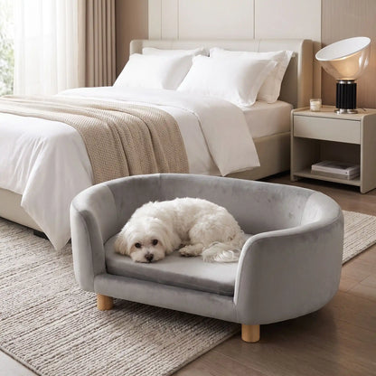 Canapé gris pour chiot et chien, structure en bois de bouleau , dossier haut et entourant à 360° au design moderne et arrondi avec son coussin en éponge 100% coton haute densité et ergonomique déhoussable et lavable en machine, housse en velours douce et résistante, sur pied en bois massif pour chien de petite taille- un petit chien blanc couché confortablement sur le canapé ergonomique au design moderne de couleur gris au pied du lit de ses maitres dans la chambre de l'appartement