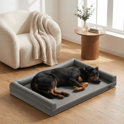 Canape-pour-chien-xxl-lit-orthopédique, matelas à mémoire de forme, 100% coton haute densité et haute résilience, accoudoir et dossier en U cylindriques, housse 100% imperméable et déhoussable, lavable, canapé lit pour grand chien de 130 cm de longueur pour grandes races de chiens jusqu'à 6 kilos maximum-un chien de grade race qui dort sur le flanc sur le canapé lit xxl anti-bactérien pour grand chien de couleur gris dans le salon moderne de l'appartement