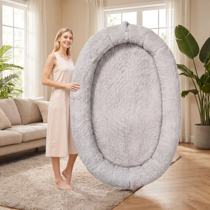 Coussin-chien-xxl-déhoussable-avec-rebord-orthopédique, matelas à mémoire de forme et rebord cylindrique surélevé 360° anti anxiété , rembourrage 100% coton PP, lit ovale en peluche, imperméable, antidérapante et lavable en machine, taille humaine pour cododo avec le chien de 176x122 cm ou couchage multi-animaux-gros plan sur le coussin gris ultra doux avec poches de rangement sur le boudin et poignée de transport mis debout à côté d'une femme adulte pour montrer l'espace xxl du coussin plus grand qu'elle