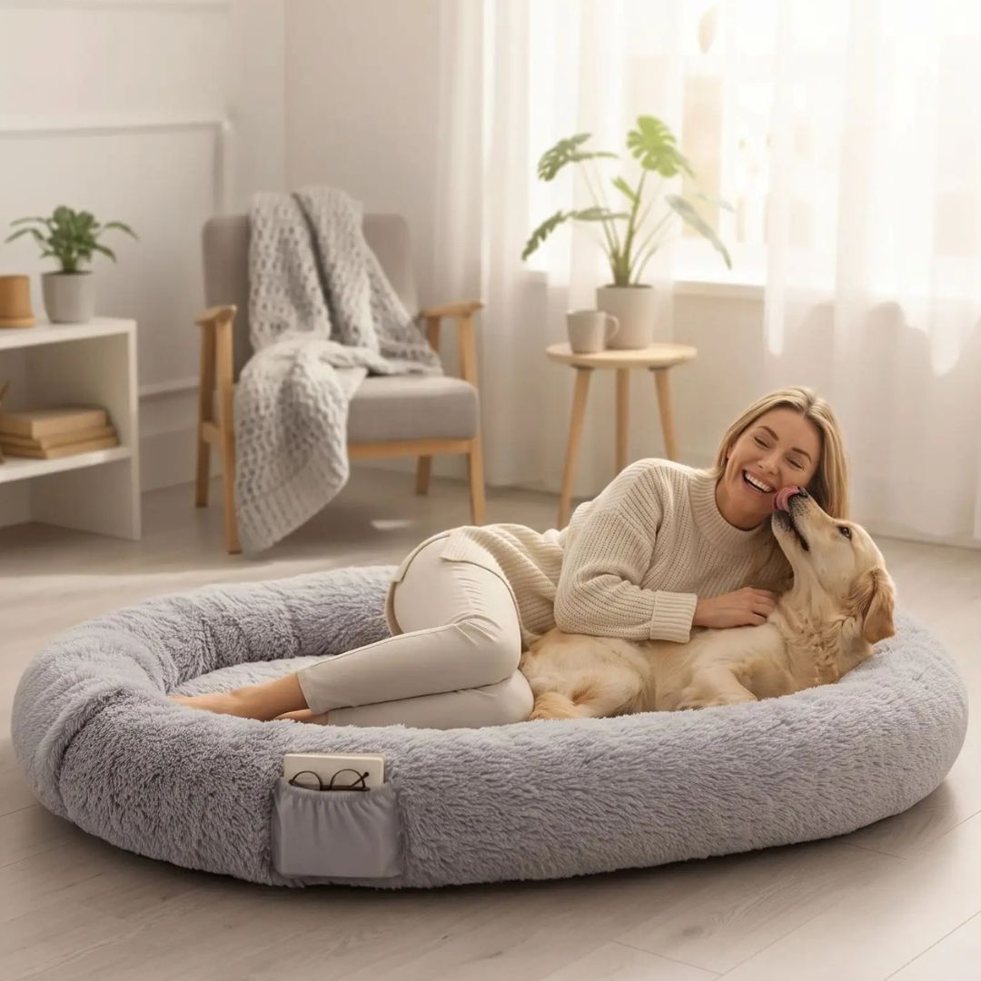 Coussin-chien-xxl-déhoussable-avec-rebord-orthopédique, matelas à mémoire de forme et rebord cylindrique surélevé 360° anti anxiété , rembourrage 100% coton PP, lit ovale en peluche, imperméable, antidérapante et lavable en machine, taille humaine pour cododo avec le chien de 176x122 cm ou couchage multi-animaux-une maitresse et son chien de grande race allongé dans le grand coussin gris ultra doux avec poches de rangement sur le boudin et poignée de transport pour une séance câlin dans la chambre 