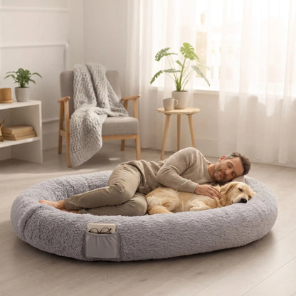 Coussin-chien-xxl-déhoussable-avec-rebord-orthopédique, matelas à mémoire de forme et rebord cylindrique surélevé 360° anti anxiété , rembourrage 100% coton PP, lit ovale en peluche, imperméable, antidérapante et lavable en machine, taille humaine pour cododo avec le chien de 176x122 cm ou couchage multi-animaux-un maitre et son chien de grande race qui dorment paisiblement niché dans le grand coussin gris ultra doux avec poches de rangement sur le boudin et poignée de transport dans la chambre de la maison