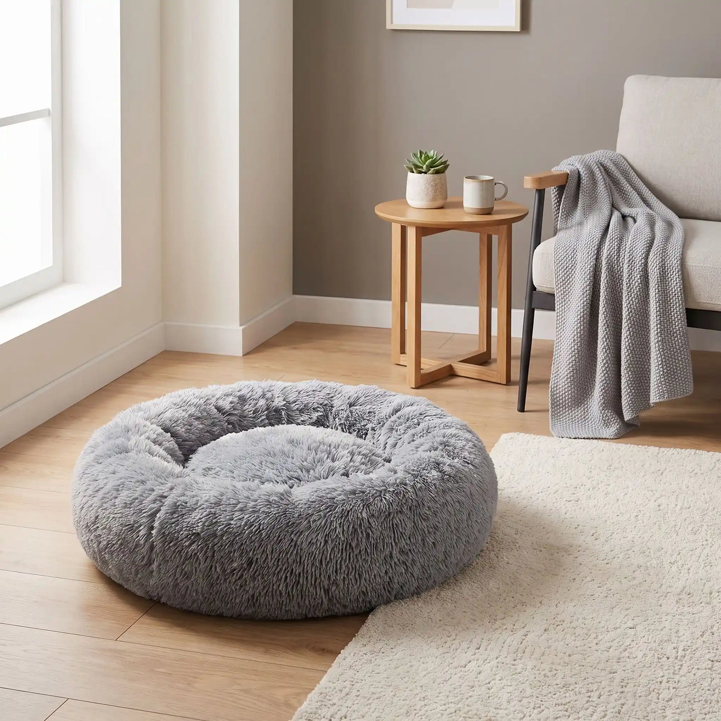 Coussin-déhoussable-pour-chien-chiot-antistress en peluche douce et hypoallergénique, lavable en machine, fond antidérapant et imperméable, en forme de beignet rond avec rebord surélevé 360°, rembourrage 100% coton haute densité, disponible en 5 tailles du S au XXL en 3 coloris rose, gris et gris foncé pour chien de 0 à 40 kg max-gros plan sur le coussin entourant et douillet de couleur  gris clair de taille XXL sur le sol de  la chambre de l'appartement