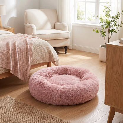 Coussin-déhoussable-pour-chien-chiot-antistress en peluche douce et hypoallergénique, lavable en machine, fond antidérapant et imperméable, en forme de beignet rond avec rebord surélevé 360°, rembourrage 100% coton haute densité, disponible en 5 tailles du S au XXL en 3 coloris rose, gris et gris foncé pour chien de 0 à 40 kg max-gros plan sur le coussin entourant et douillet de couleur rose de taille XXL sur le sol de  la chambre de l'appartement