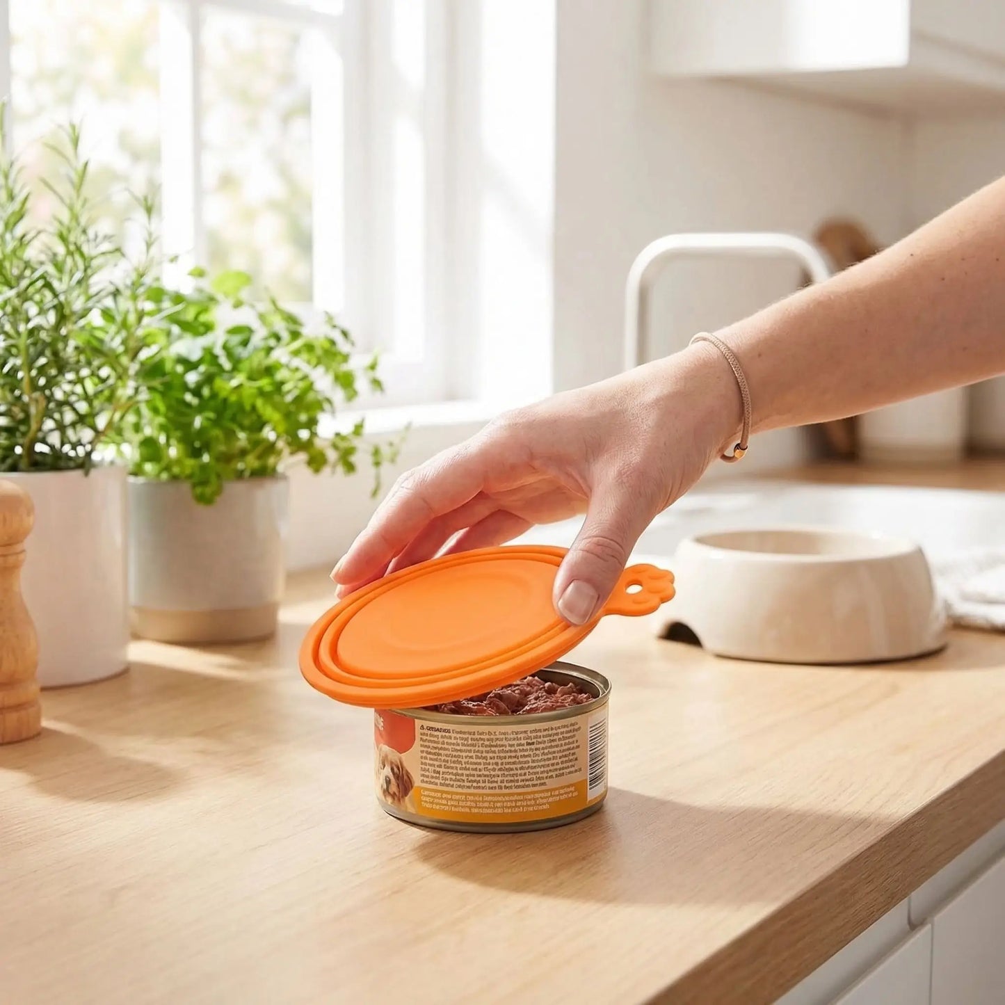 Couvercles-pour-boite-de-conserve-adaptable-universel pour toutes tailles de conserve de pâté ou nourriture pour chien ou chats-réutilisable et lavable en lave vaisselle, vendus par lot de 5 couvercles-une femme qui ferme la boite de pâté de son petit chien avec le couvercle de couleur orange avec 3 circonférences adaptables pour toute tailles de conserve qur le plan de la cuisine pour une bonne conservation qui évite les odeurs et favorise l'hygiène alimentaire