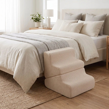 Escalier-pour-chien-2-en-1- transformable en rampe douce-en-mousse- tissu antidérapant, déhoussable et lavable en machine, éponge coton haute densité et élasticité qui absorbe les chocs, protège les articulations et la colonne vertébrale, léger et transportable, adapté au chiot et chien de race petite à moyenne, disponible en 3 couleurs beige, gris clair et gris foncé-gros plan sur l'escalier en version 3 marches de couleur beige contre le lit  deux places dans la chambre de l'appartement