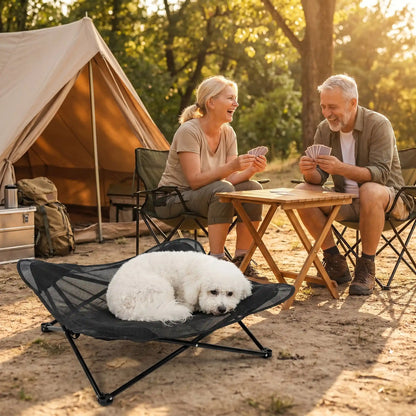 Fauteuil-pour-petit-chien-camping-chaise pour chien beige ou noir, lit de camp carré avec tissu déhoussable imperméable et lavable, en maille respirante pour un lit rafraichissant en été structure en acier inoxydable solide et pliant pour une utilisation partout en intérieur et extérieur pour chiot et chien de petite race de 0 à 5 kilos-un chien de petite taille qui dort couché en boule au frais sur son lit de camp à côté de ses maitres qui jouent aux cartes devant leur tente dans le camping en forêt en été