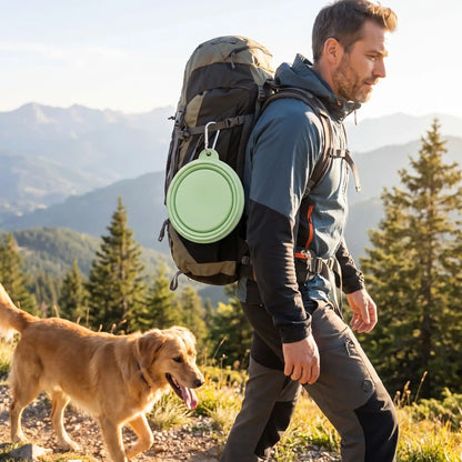 Gamelle-pliable-chien-chiot-lot-de-2-en silicone alimentaire, garanti sans produits chimiques, lavable en lave-vaisselle, robuste et compact comme un CD avec son mousqueton pour l'accrocher n'importe où, léger avec ses 80g, disponible en 2 tailles 350ml et 1000 ml pour toutes races de chien et trois couleur : rose, bleu et vert-un maitre qui porte son sac à dos avec la gamelle pliable attaché dessus par son mousqueton solide avec son chien pour une randonnée en montagne