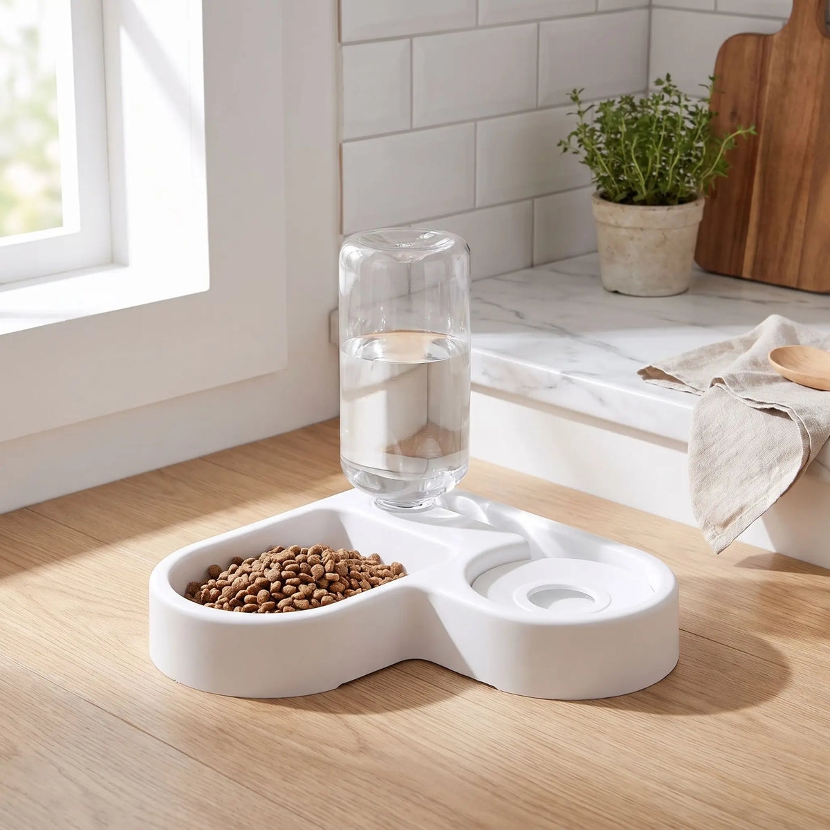 Gamelle-pour-petit-chien et chiot avec double avec séparateur alimentation et eau, distributeur d'eau de 500 ml automatique et gamelle hygiénique en forme design de couleur blanche et réservoir d'eau transparent , matériaux sûr en PP de qualité alimentaire, robuste et sans BPA, lavable et antidérapant- un gros plan sur la gamelle double avec deux gamelles pour eau et nourriture avec son distributeur d'eau automatique et hygiénique de couleur blanc sur le meuble de la cuisine