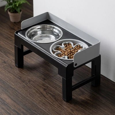 Gamelles surélevées gris et noir réglable sur 5 hauteurs, de 21/23/25/27/28 cm avec rebord anti-éclaboussure et anti-débordement, disponible en 2 modèles, matériaux ABS robuste noir et 2 gamelles inox ou 1 gamelle inox et gamelle anti-glouton, station d'alimentation inclinable par 5° pour chiot en croissance ou chien de petite à moyenne taille- gros plan sur la station d'alimentation et sa gamelle d'eau de 1L en inox et sa gamelle anti glouton remplie de croquettes contre le mur du salon de la maison