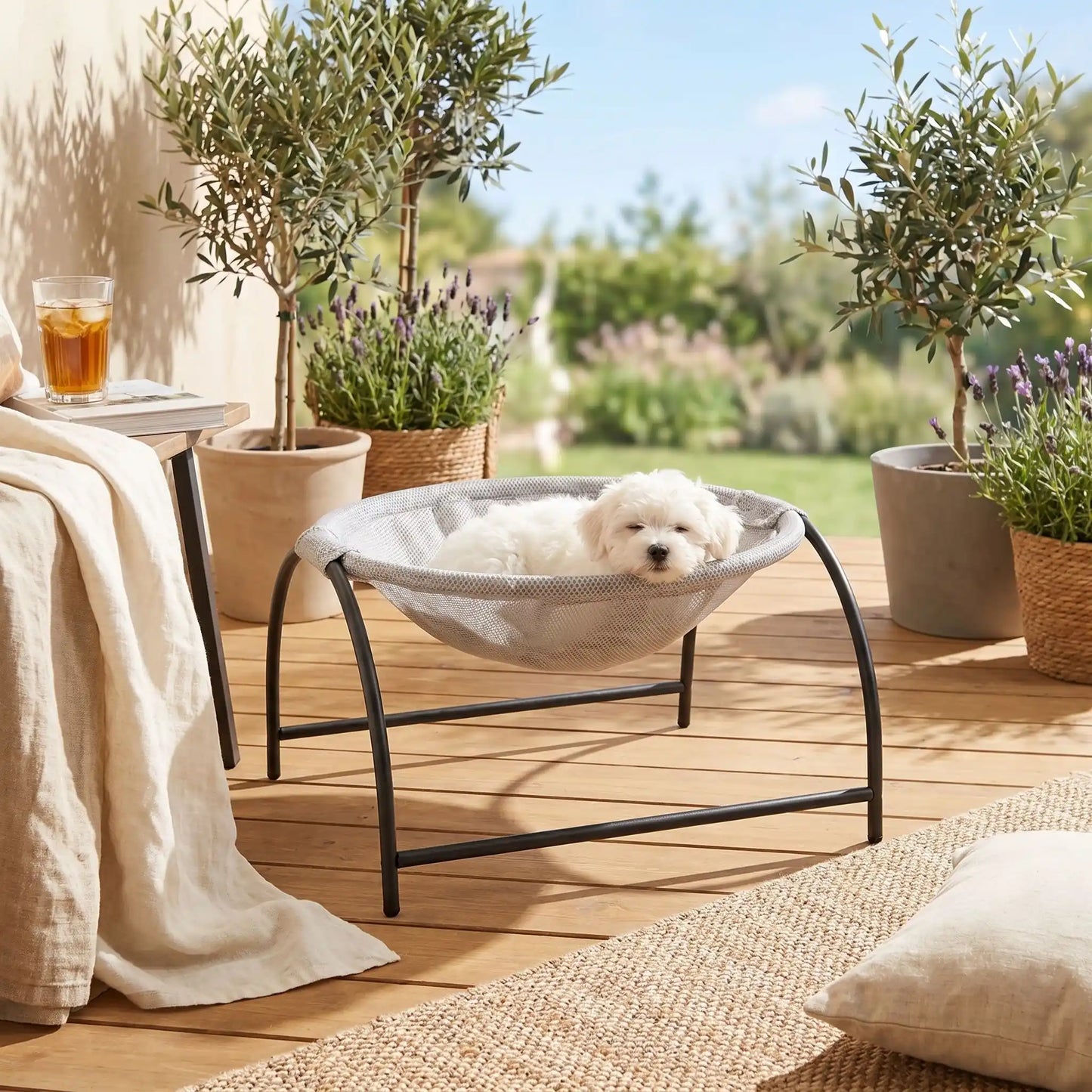 Hamac-pour-chien-chiot-exterieur et interieur en maille respirante et hypoallergénique, structure solide en acier avec 3 pieds et renfort par de barres latérales, cerceau central entourant et apaisant pour les chiot et chien de petite taille et de races naines de 0 à 3 kilos max , imperméable et lavable-un chiot bichon maltais qui dort paisiblement niché dans son hamac rond gris entourant avec sa structure en acier sur la terrasse su jardin de la maison a soleil en été
