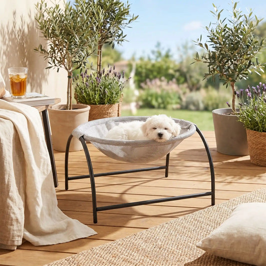 Hamac-pour-chien-chiot-exterieur et interieur en maille respirante et hypoallergénique, structure solide en acier avec 3 pieds et renfort par de barres latérales, cerceau central entourant et apaisant pour les chiot et chien de petite taille et de races naines de 0 à 3 kilos max , imperméable et lavable-un chiot bichon maltais qui dort paisiblement niché dans son hamac rond gris entourant avec sa structure en acier sur la terrasse su jardin de la maison a soleil en été