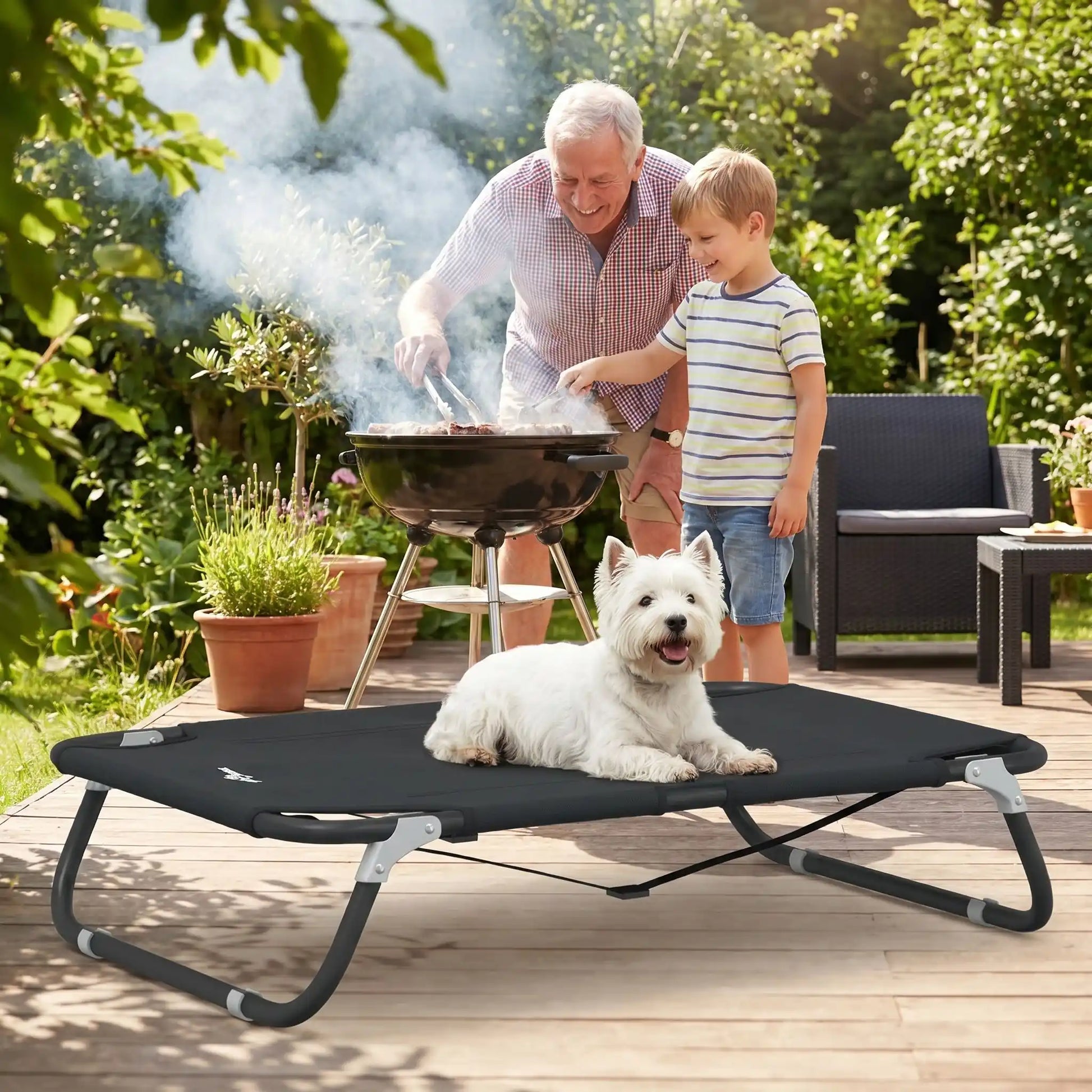 Lit-pliant-chien-chiot-pour race de petite taille et races naines de 0 à 10 kilos, tissu oxford doux, imperméable, lavable et résistante qui épouse le corps du chien ou du chiot comme un hamac avec structure rectangulaire en acier avec deux barres transversales mobile pour un pliage facile et rapide pour une utilisation en intérieur ou extérieur-un petit chien confortablement couché sur le lit surélevé de couleur noir dans le jardin à côté de son maitre et son petit fils qui font un barbecue dans le jardin 