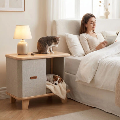 Meuble-niche-chien-interieur-chiot-design- en bois massif d'hêtre et de pin robuste avec son coussin interieur en lin écologique épais rembourré 100% coton PP amovible et lavable, bords arrondis anti-blessure sur 4 pieds robustes en bois, matériaux 100% naturels de couleur marron clair et beige, format compact, idéal pour les petits espaces, imperméable-un chiot  qui dort en boule paisiblement dans le meuble niche design et un chat assis sur le dessus du meuble qui se lèche à côté du lit de leur maitresse 