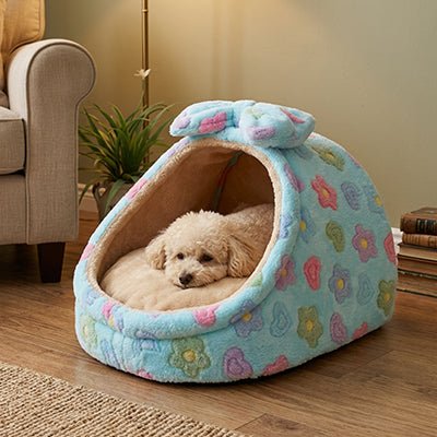 Panier-chien-niche-cocon-avec-coussin ergonomique et amovible, panier anti-stress 100% coton haute densité, lavable en machine, antidérapant avec toit , enveloppant, protège du sol froid et des courant d'air pour les chiots et chiens de race naine ou  petite taille de 0 à 5 kilos-un chien de petite race couché confortablement au chaud et en sécurité dans son panier niche design floral avec son noeud sur le toit décoratif sur le sol du salon de l'appartement