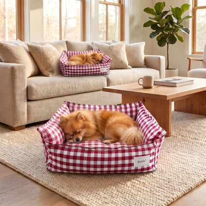 Panier-petit-chien-et-chiot-carreaux-vichy, 100% déhoussable,housse coton respirante 100% coton à carreaux vichy, coussin intérieur et 3 boudin au rembourrage 100% coton pour un panier confortable et ergonomique, anti-anxiété pour chiot chien de petite race et petite taille, disponible en 2 tailles XS et S-un loulou de poméranie qui dort paisiblement dans son panier coussin rembourré avec rebords surélevés au rembourrage 100% coton haute densité avec motif carreaux vichy rouge et blanc dans le salon