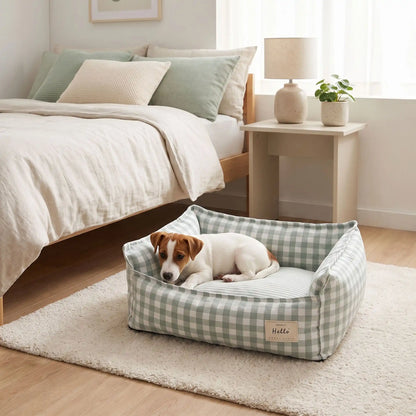 Panier-petit-chien-et-chiot-carreaux-vichy, 100% déhoussable,housse coton respirante 100% coton à carreaux vichy, coussin intérieur et 3 boudin au rembourrage 100% coton pour un panier confortable et ergonomique, anti-anxiété pour chiot chien de petite race et petite taille, disponible en 2 tailles XS et S-un chiot jack russell niché confortablement dans son panier coussin rembourré avec rebords surélevés avec motif carreaux vichy rouge et blanc au pied du lit de ses maitres sur le sol de la chambre 