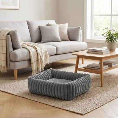 Panier-petit-chien-chiot-velours-confortable rectangulaire en velours ultra doux et résistant avec rebord 360° surélevé pour un effet cocon apaisant et rassurant anti-stress pour chien de petite taille de 0 à 9 kilos max, lavable en machine,épais rembourrage 100% Coton haute densité, fond imperméable et antidérapant-gros plan sur le panier pour petit chien et chiot rectangulaire  douillet et rembourrage généreux 100% coton haute résilience de couleur gris foncé sur le sol du salon de l'appartement