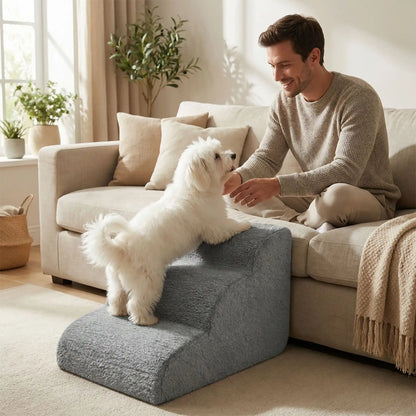 Petit-escalier-pour-chien-anti-deformationen mousse éponge haute résilience qui atténue la pressions sur  ses articulations, résistant et doux pour ses coussinets, déhoussable et lavable en machine de couleur gris pour chien de petite taille, polyvalent compact et transportable-un chien blanc à poils longs qui monte sur l'escalier pour rejoindre son maitre qui le regarde en souriant assis sur le canapé du salon de la maison