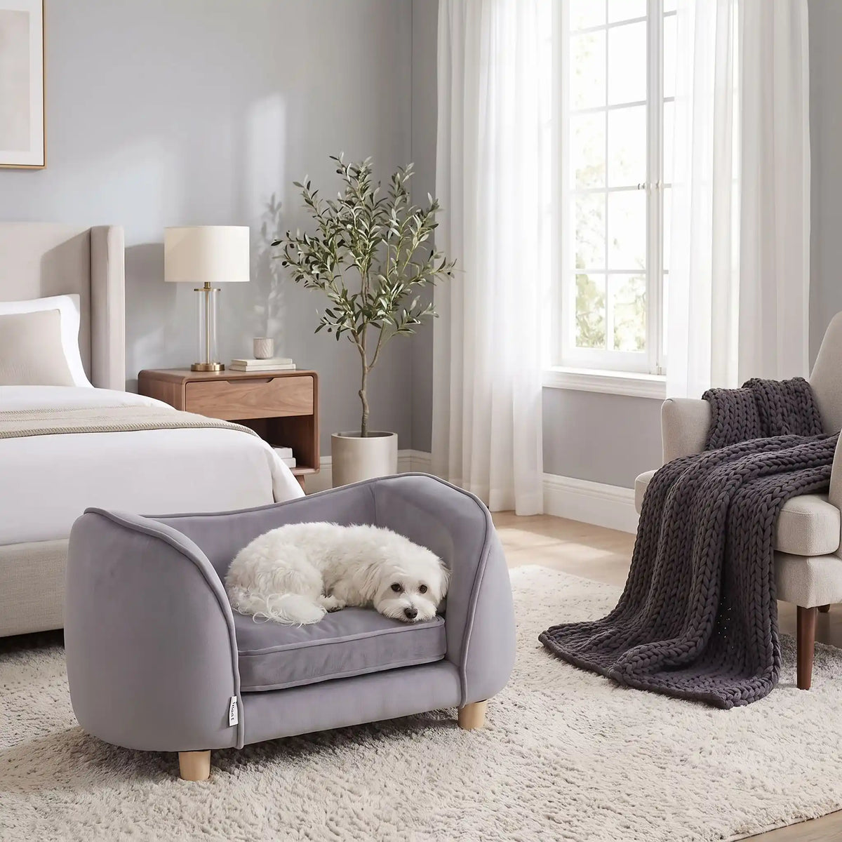 Petit-fauteuil-pour-chien-chiot-coussin intérieur épais au rembourrage 100% coton ergonomique, velours doux et résistant aux griffes, imperméable déhoussable et lavable en machine, de couleur gris, au design enveloppant en forme bateau structrure en bois massif avec 4 pieds à vissés en bois massif et robuste pour chiot et chien de petite taille à moyenne taille-un chien de petite taille qui dort paisiblement enveloppé dans son fauteuil avec son haut dossier au pieds du lit de ses maitres dans la chambre