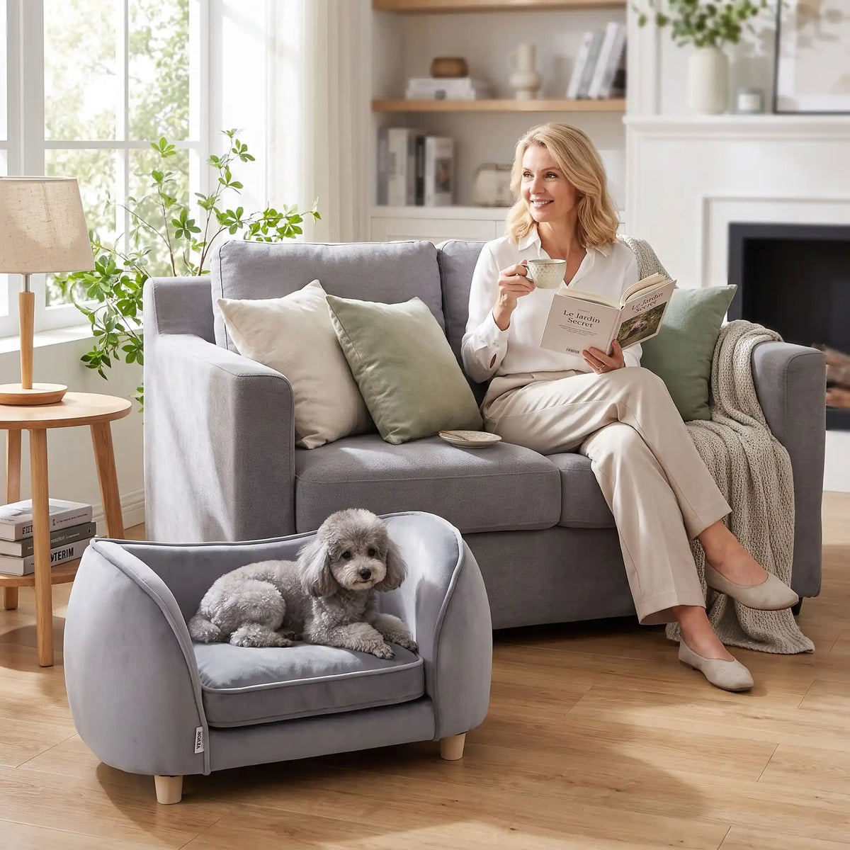 Petit-fauteuil-pour-chien-chiot-coussin intérieur épais au rembourrage 100% coton ergonomique, velours doux et résistant aux griffes, imperméable déhoussable et lavable en machine, de couleur gris, au design enveloppant en forme bateau structrure en bois massif avec 4 pieds à vissés en bois massif et robuste pour chiot et chien de petite taille à moyenne taille-un chien de race moyenne couché confortablement niché dans son fauteuil gris avec son haut dossier au pied de sa maitresse assise dans son canapé 