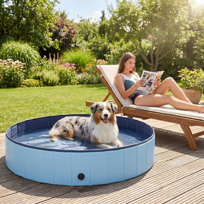 Piscine-pour-gros-chien-rigide-xxl, panneaux MDF robuste anti-affaissement, pliable et lavable de diamètre 160 cm et de 30 cm de hauteur étudié pour une entrée et sortie facile et sécurisé pour le chien avec bouchon de vidange pratique et rapide, polyvalente piscine à balle, bassin, baignoire pour toilettage-un Berger australien couché  confortablement au frais dans l'eau de la grande piscine robuste pour chien de couleur bleu sur la terrasse du jardin à côté de sa maitresse sur un transat en eté