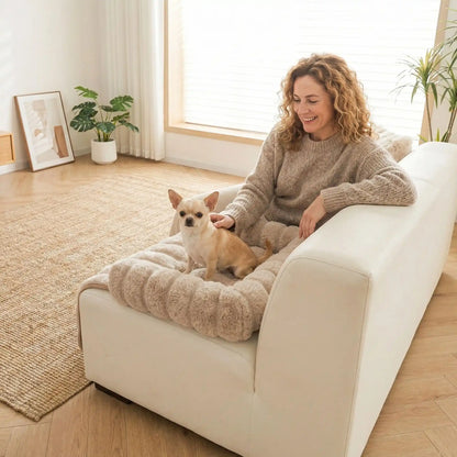 Protection-canape-chien-lit-antiderapant avec traversin entourant sur 3 côté, en fausse fourrure rembourrage 100% coton haute densité, polyvalent pour le sol, canapé, protège lit, portège siège voiture, tapis de cage, pliable, léger et portable pour petit à chien moyenne taille-dimensions 75x75 cm-un chien de race naine confortablement assis sur le protège canapé pour chien en fausse fourrure douce de couleur marron clair avec traversin rembourré caresser par sa maitresse assise sur le canapé à côté de lui