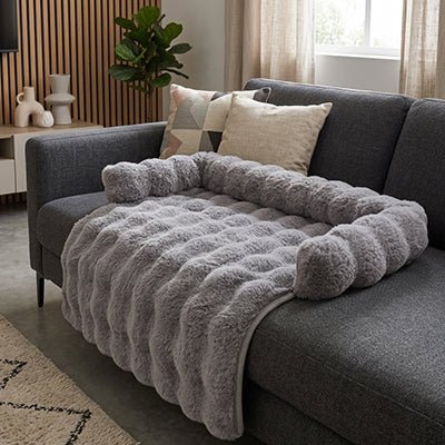 Protection-canape-chien-lit-antiderapant avec traversin entourant sur 3 côté, en fausse fourrure rembourrage 100% coton haute densité, polyvalent pour le sol, canapé, protège lit, protège siège voiture, tapis de cage, pliable, léger et portable pour petit à chien moyenne taille-dimensions 75x75 cm-gros plan sur le protège canapé et literie de couleur gris foncé avec son traversin rembourré 100% cototn haute densité sur le canapé du salon de l'appartement