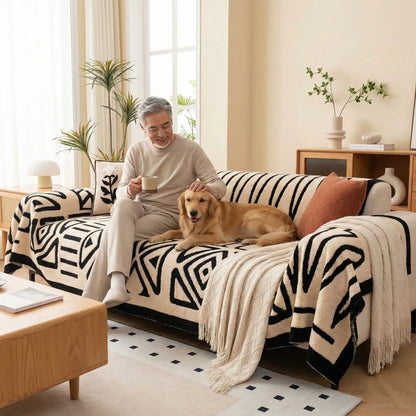 Protection-canape-chien-chiot-plaid chaud et épais, antidérapant et coutures solides, lavable en machine à laver avec design déométrique moderne pour couvrir et protéger le canapé, lit ou mobilier des poils et tâches des chiens, écoresponsable et résistantes aux griffes-un grand chien couché sur la protection canapé blanc crème aux motifs géométriques noir avec son maitre qui le caresse tendrement assis à côté de lui sur le canapé du salon de la maison