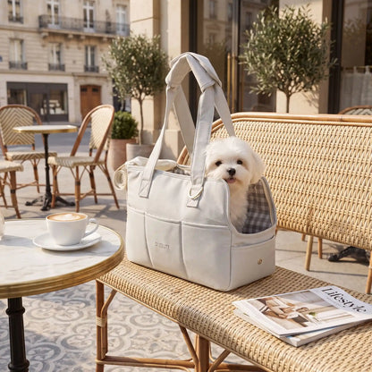 Sac-de-transport-chien-chiot- design sac à main avec multiples poches pour chien de 0 à 6 kg max,imperméable, coussins intérieur 100% coton lavable et rembourré, deux sangles avec poignées confort rembourré et renforcé pour être porté à la main ou sur l'épaule, attache laisse intégré pour sa sécurité et fillet refermable sur le so et ouverture latéral pour qu'il passe sa tête-gros plan sur le sac de transport avec un petit chien assis dedans posé sur le banc de la terrasse du café en été