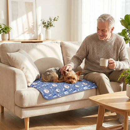 Tapis-pour-chiens-100% imperméable, 100 %coton haute densité lavable en machine, polyvalent, solide et résistant aux griffes, rafraichissant pour l'été et confortable en hiver, protège vos sols et vos meubles, disponible en 4 tailles du XS au L pour chiot et chien de petite à moyenne taille de 0 à 25 kg avec motif mignon-un Yorkshire couché confortablement sur son tapis bleu avec motif mignon qui protège le canapé où son maitre le caresse assis à côté avec sa tasse de café dans l'autre main dans le salon 